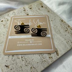 a pair of black and gold earrings sitting on top of a piece of white paper