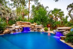 an outdoor pool with waterfall and water features surrounded by palm trees, shrubs and other greenery