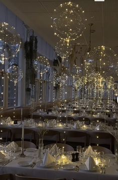 a dining room filled with lots of tables covered in white tablecloths and lighted chandeliers