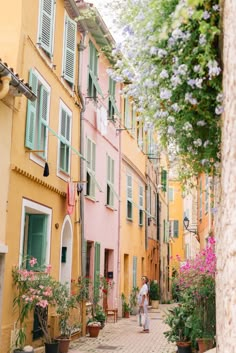 a person walking down an alley way in front of colorful buildings with green shutters