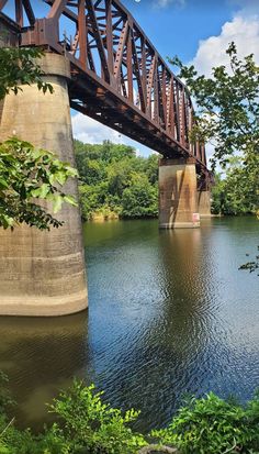 a bridge over a body of water with trees and bushes around it on a sunny day