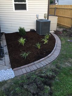 an air conditioner sitting on the side of a house next to a flower bed