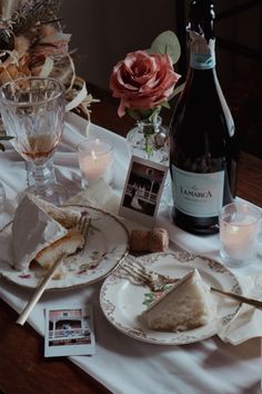 a table topped with plates covered in food next to a bottle of wine and candles