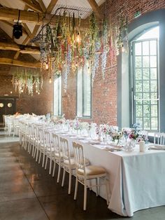 a long table is set up with white linens and flowers hanging from the ceiling