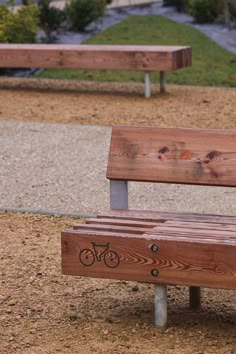 a wooden park bench sitting on top of a dirt field next to a bike path