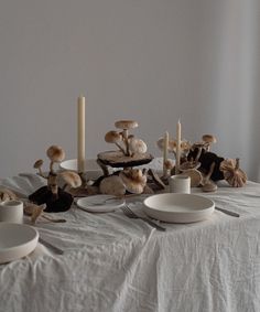 a table topped with plates and mushrooms next to candle holders on top of a white cloth covered table