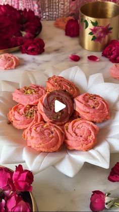 pink cookies are arranged on a white platter with flowers in the background and a gold cup