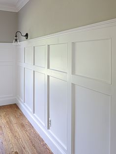 an empty room with white paneling and wood floors