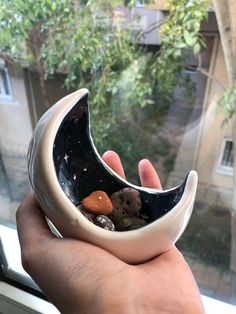 a hand holding a black and white bowl with rocks in it