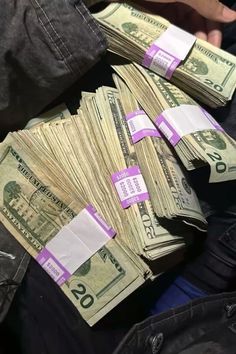 a pile of money sitting on top of someone's lap with their hands over them