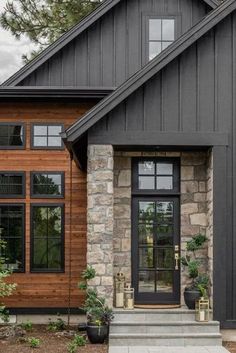 a black and brown house with stone steps leading up to the front door that has two potted plants on each side