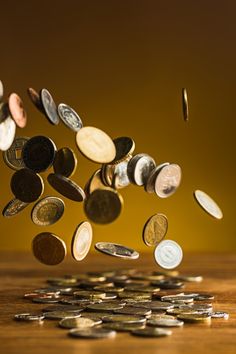 a person throwing coins into the air on top of a wooden table in front of a yellow background