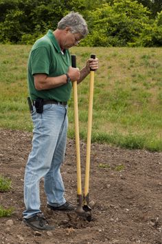 a man holding two large yellow shovels in his hands while standing on the ground