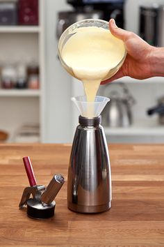 a person pours liquid into a coffee pot on top of a wooden countertop