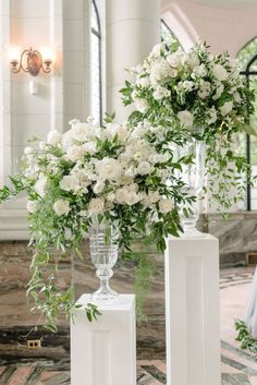 two tall white vases with flowers in them sitting on the floor next to each other