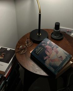 a table with a lamp, book and eyeglasses on it next to a stack of books