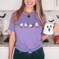 a woman is holding two mugs in her hands while wearing a t - shirt with three ghost faces on it