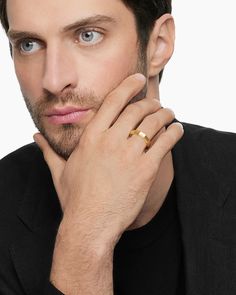 a man in a black suit and gold ring looking at the camera with his hand on his chin