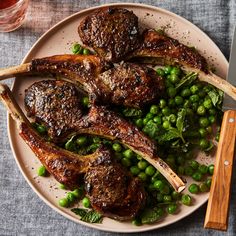 a plate with meat and peas on it next to a fork, knife and spoon