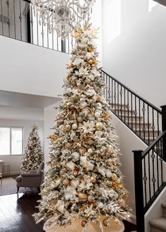 a white christmas tree with gold and silver decorations in a living room under a chandelier