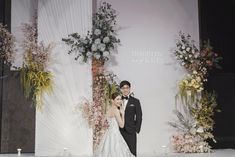 a man and woman standing on a runway in front of floral displays at a fashion show