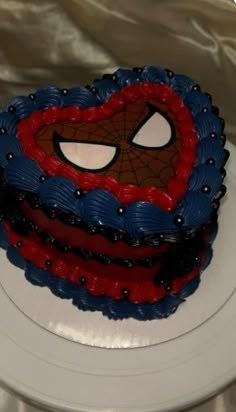 a spiderman cake on a white plate with silver cloth behind it and the top layer is red, blue, and black