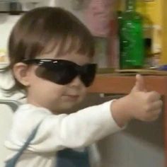 a young child wearing sunglasses and pointing at something on the shelf in front of him