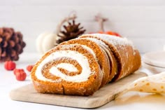 a cinnamon roll with cream cheese frosting on a cutting board next to pumpkins and pine cones