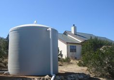 a large white tank sitting in front of a house on a dirt lot next to trees