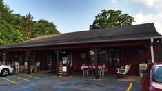 a car parked in front of a red building with tables and chairs on the outside