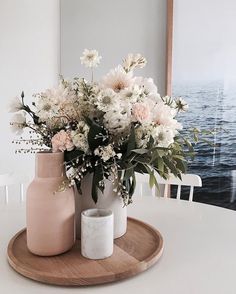 two vases with flowers in them sitting on a wooden tray next to the ocean