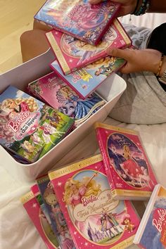 there are many children's books in the box on the bed and someone is holding one