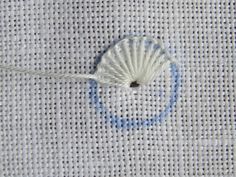 a white piece of cloth with a blue circle on it and some thread in the middle