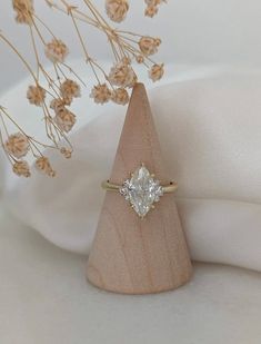 a diamond ring sitting on top of a piece of wood next to some dried flowers