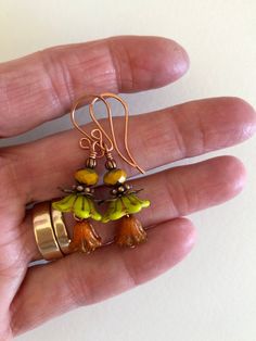 "Adorable new Czech glass premium flower earrings in chartreuse green and orange opaline with mustard yellow and copper accents. Opaque chartreuse Czech glass bellflowers with copper Picasso finish are accented with little Czech glass lilies in burnt orange opaline with metallic copper wash and mustard yellow Picasso rondelles. Wire wrapped in bright copper with copper accents. Ear wires are handmade German copper. Total drop is 1 3/4\"." Nickel-free Yellow Czech Glass Earrings, Nickel Free Yellow Czech Glass Earrings, Orange Flower-shaped Adjustable Earrings, Yellow Czech Glass Earrings For Gifts, Yellow Glass Earrings For Gift, Green Flower-shaped Glass Jewelry, Green Glass Flower-shaped Jewelry, Green Czech Glass Flower Earrings, Unique Yellow Czech Glass Jewelry