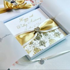 two wedding cards in a white box with gold ribbon and bow on the front, sitting next to each other