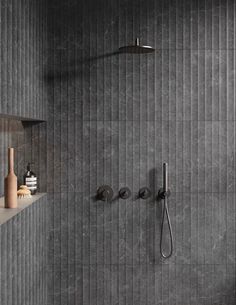 a bathroom with grey tile and black fixtures on the wall, along with a shower head