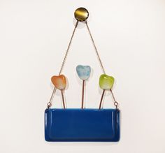 three candy lollipops in a blue container hanging from a chain on a white wall