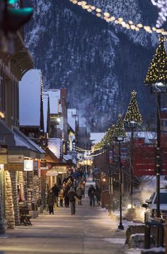 people are walking down the street in front of buildings with christmas lights strung across them