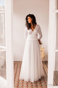 a woman in a white dress is standing by a window