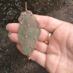 a person is holding a green piece of glass in their left hand and gold wire around it