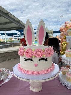 a white cake with pink frosting and bunny ears on top sitting on a table