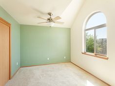 an empty room with green walls and a ceiling fan in the corner near a window