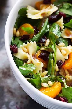 a white bowl filled with pasta and spinach salad on top of a marble table