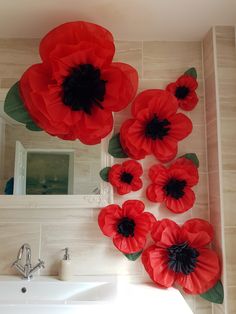 red paper flowers are hanging on the wall above a white sink in a tiled bathroom