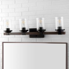 a bathroom vanity light with five candles on the top and mirror above it in front of a white brick wall