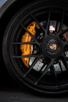 the front wheel of a sports car with black spokes and yellow brake pads on it