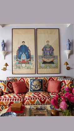 two paintings on the wall above a couch with pillows and flowers in front of it