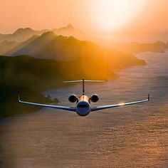 an airplane is flying over the water and mountains at sunset or sunrise with sunbeams in the sky