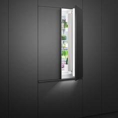 an open refrigerator door with the light on in a dark, empty kitchen area that appears to be painted black